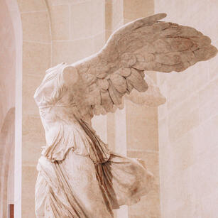 A white marble statue of a human figure with angel wings. The figure has no head or arms.